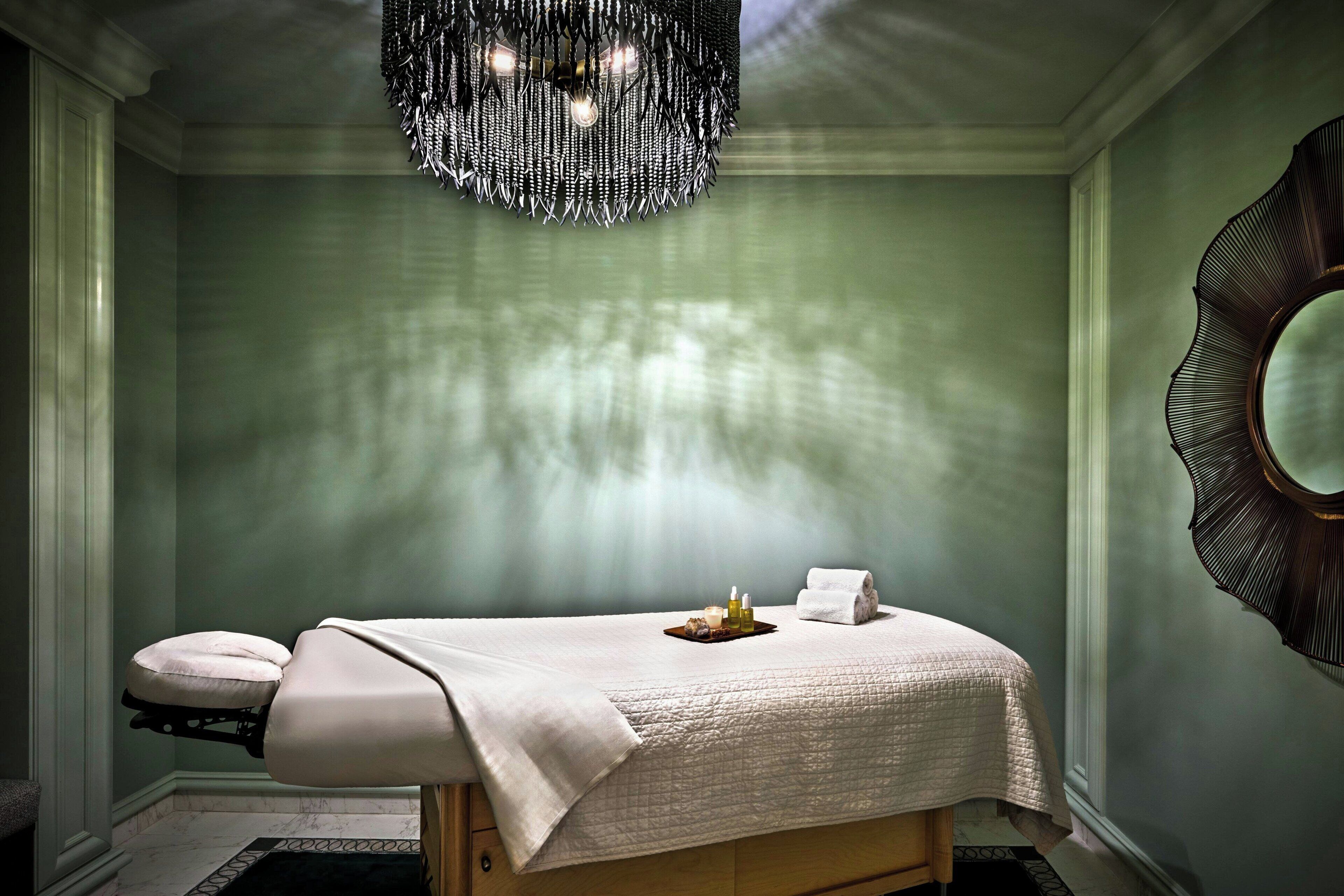 A spa room with a massage table, a decorative mirror, and a chandelier.