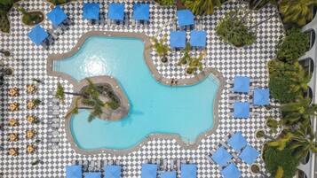 Vista aérea de un complejo turístico con una piscina central rodeada de suelo a cuadros, sillones de descanso y sombrillas.
