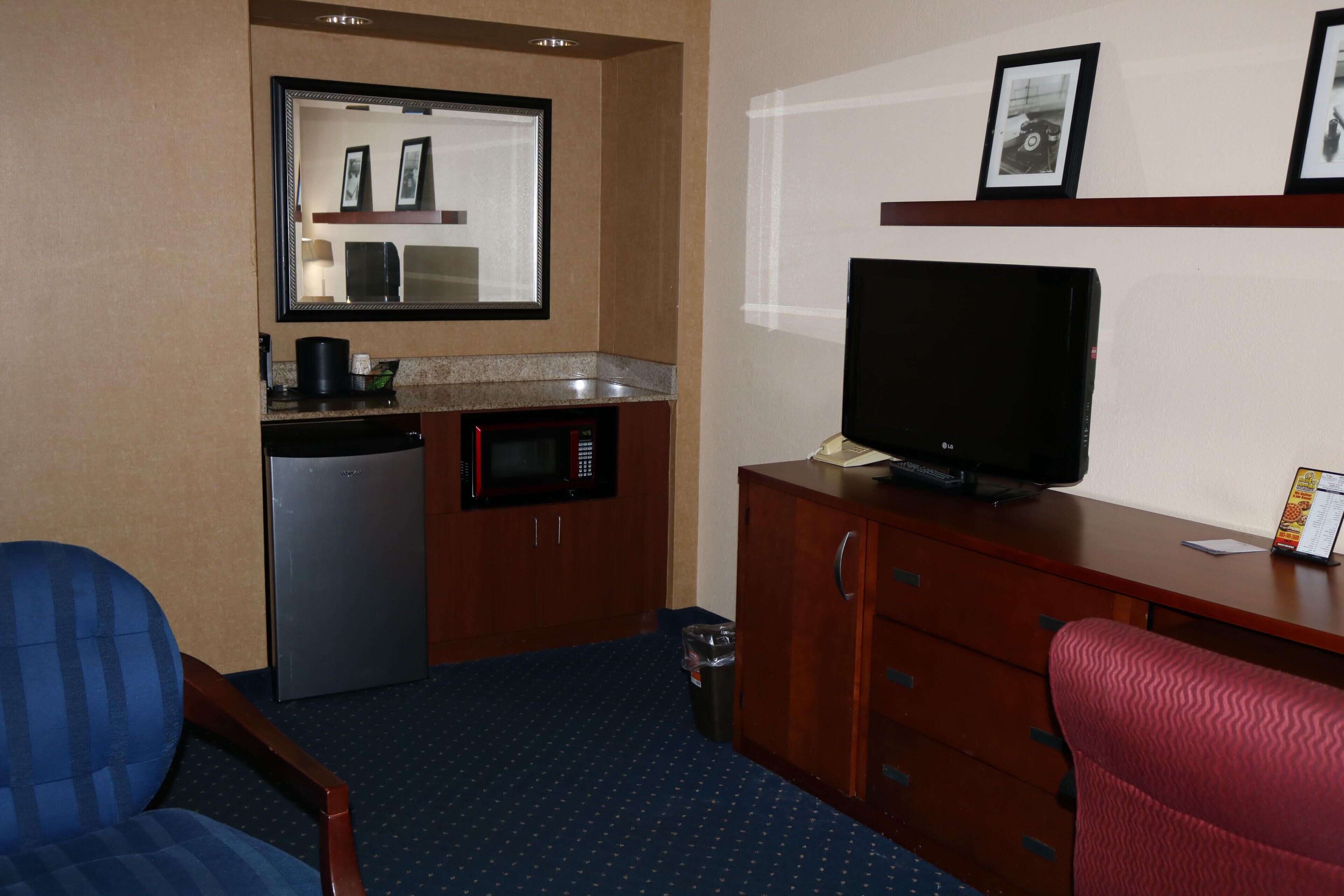 Una habitación de hotel compacta con kitchenette, televisión, una silla azul y una silla roja.