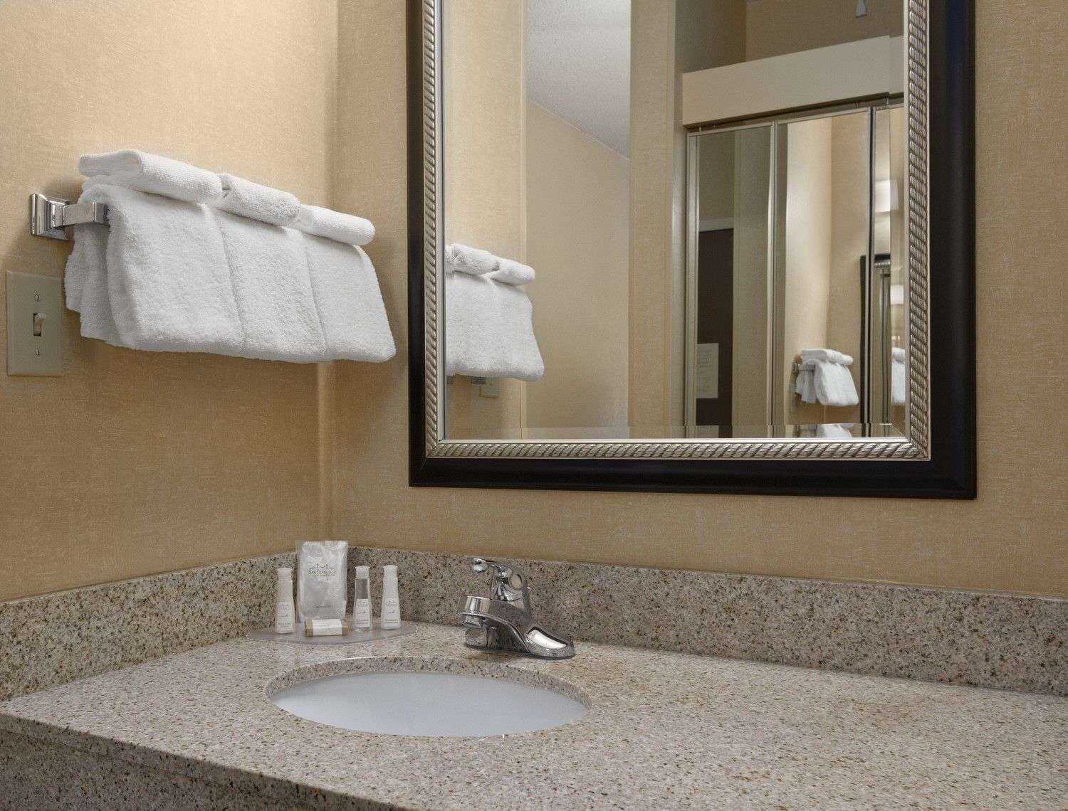 A bathroom with a granite countertop sink, a mirror, and two white towels hanging on a towel rack.