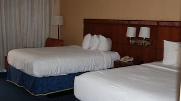 A hotel room with two beds, a nightstand with a phone, and a lamp.