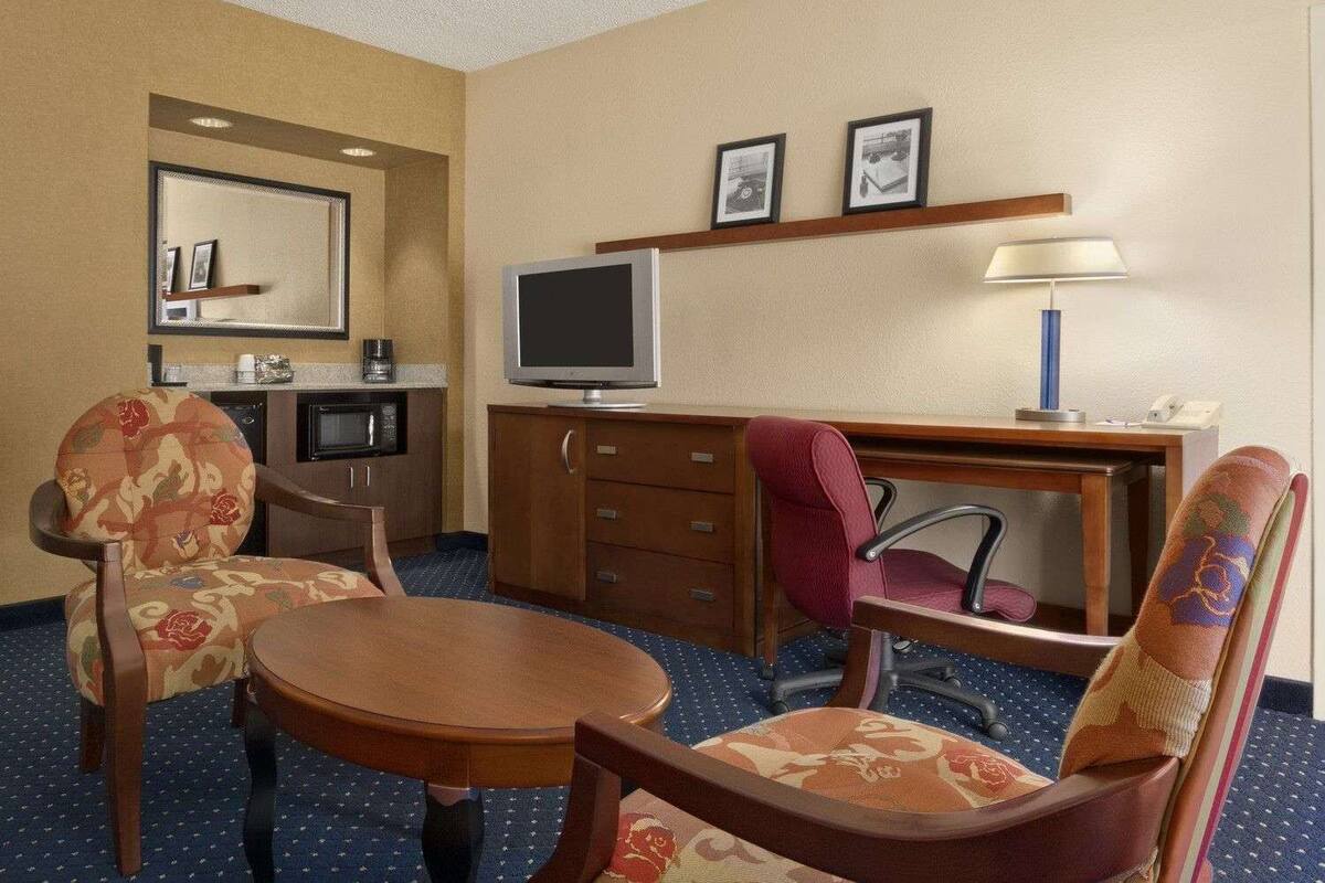 A hotel room with a dining table, two chairs, a television, a desk with a lamp, a microwave, and a coffee maker.