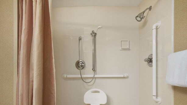 Ein Badezimmer mit bodengleicher Dusche, Haltegriff und Toilette in Weiß.