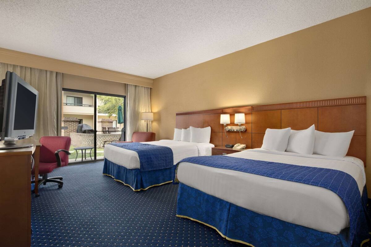 A hotel room with two beds, a desk with a computer, a chair, and a view of the outdoors.