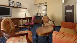 Hotelkamer met een bureau, twee fauteuils, een bank, een televisie, een koffiezetapparaat en een spiegel.