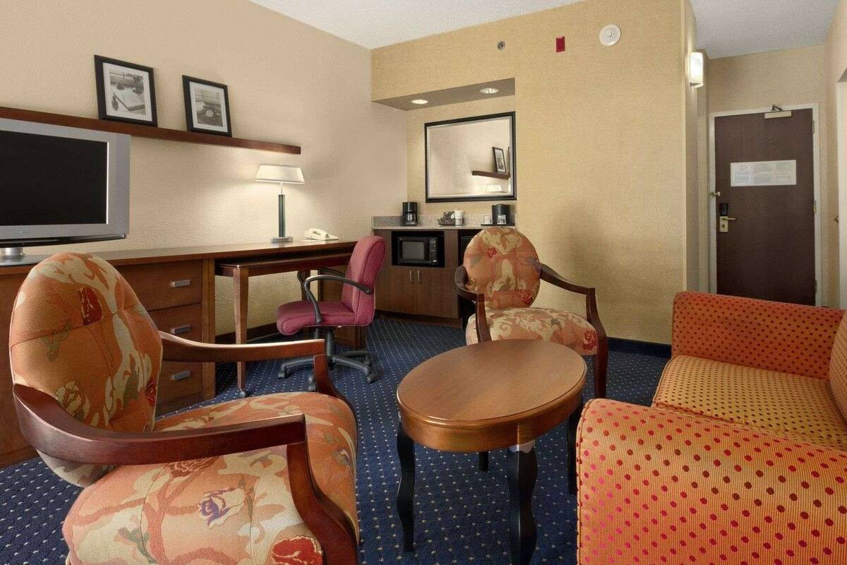 A hotel room with a desk, two armchairs, a sofa, a television, a coffee maker, and a mirror.