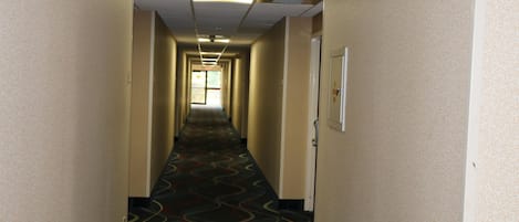 Un pasillo de hotel con alfombra estampada, paredes color beige y una puerta al final.