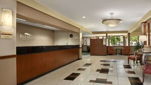 Een hotel receptie met een Baymont Inn & Suites bord, een receptiebalie, een klok en een zithoek met stoelen en een tafel.