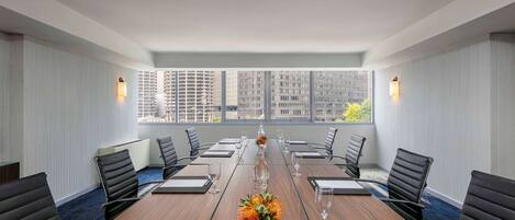 A conference room with a long table, black chairs, and a vase of flowers.