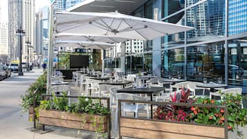 An outdoor cafe with tables and chairs, surrounded by planters with flowers.