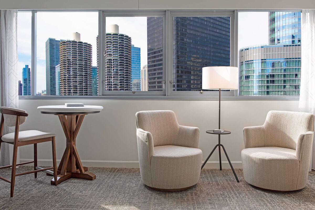 A room with a city view, two armchairs, a small round table, and a floor lamp.