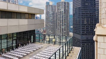 Terraza en la azotea con mesas y sillas, con vistas a un paisaje urbano de edificios altos.
