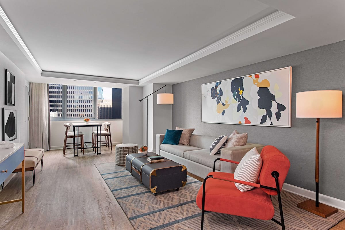 A modern living room with a sofa, a red armchair, a coffee table, and a dining area with a table and chairs.