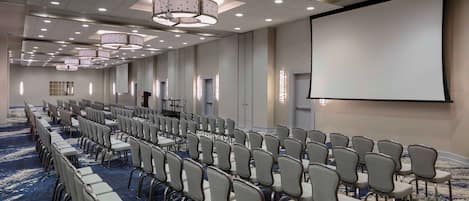 A conference room with rows of chairs, a large screen, and a carpeted floor.