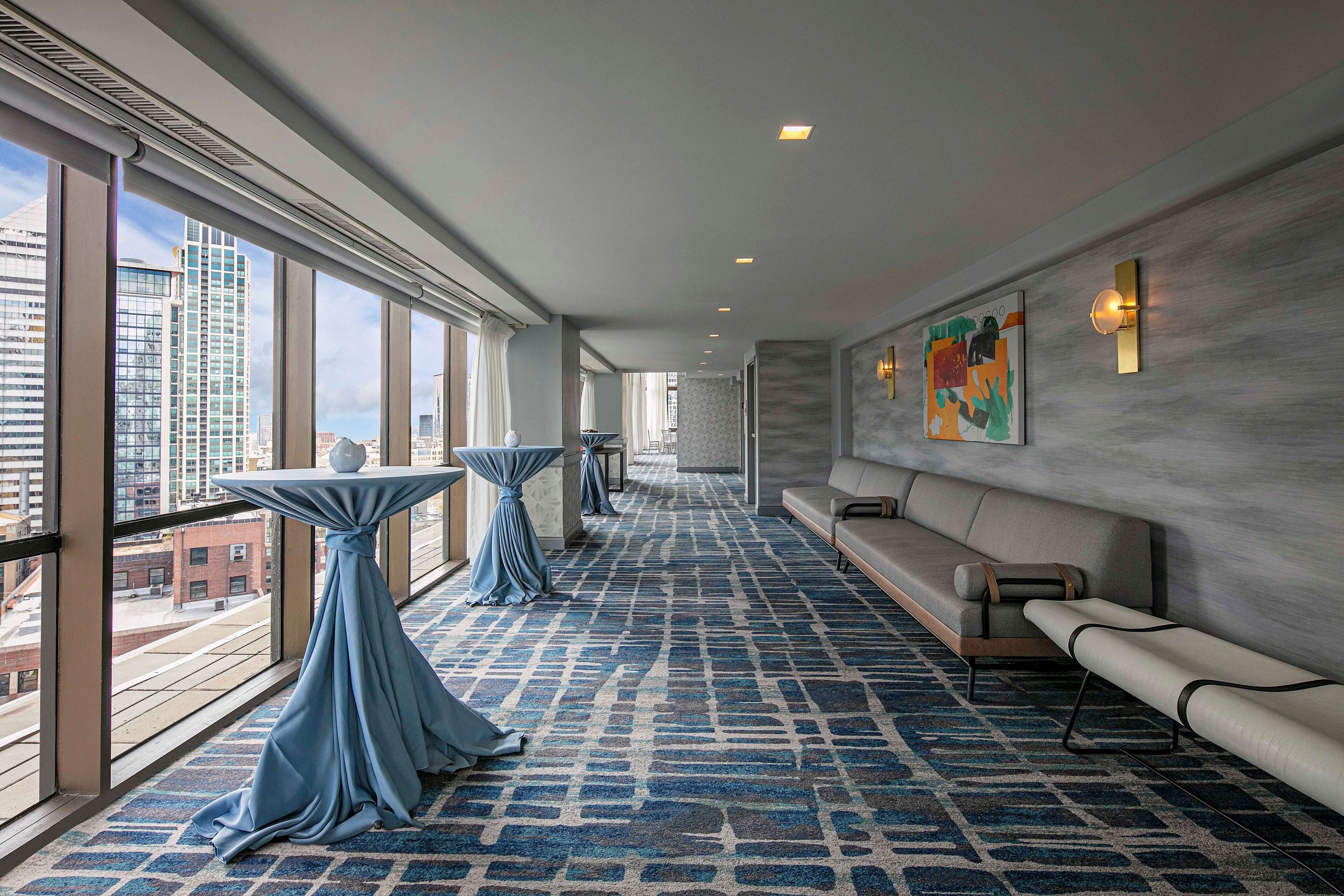 Een moderne hotel lobby met grote ramen, een kamerbreed tapijt, een bank en een tafel met een gedrapeerd tafelkleed.