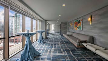 A modern hotel lobby with large windows, a patterned carpet, a sofa, and a table with a draped tablecloth.
