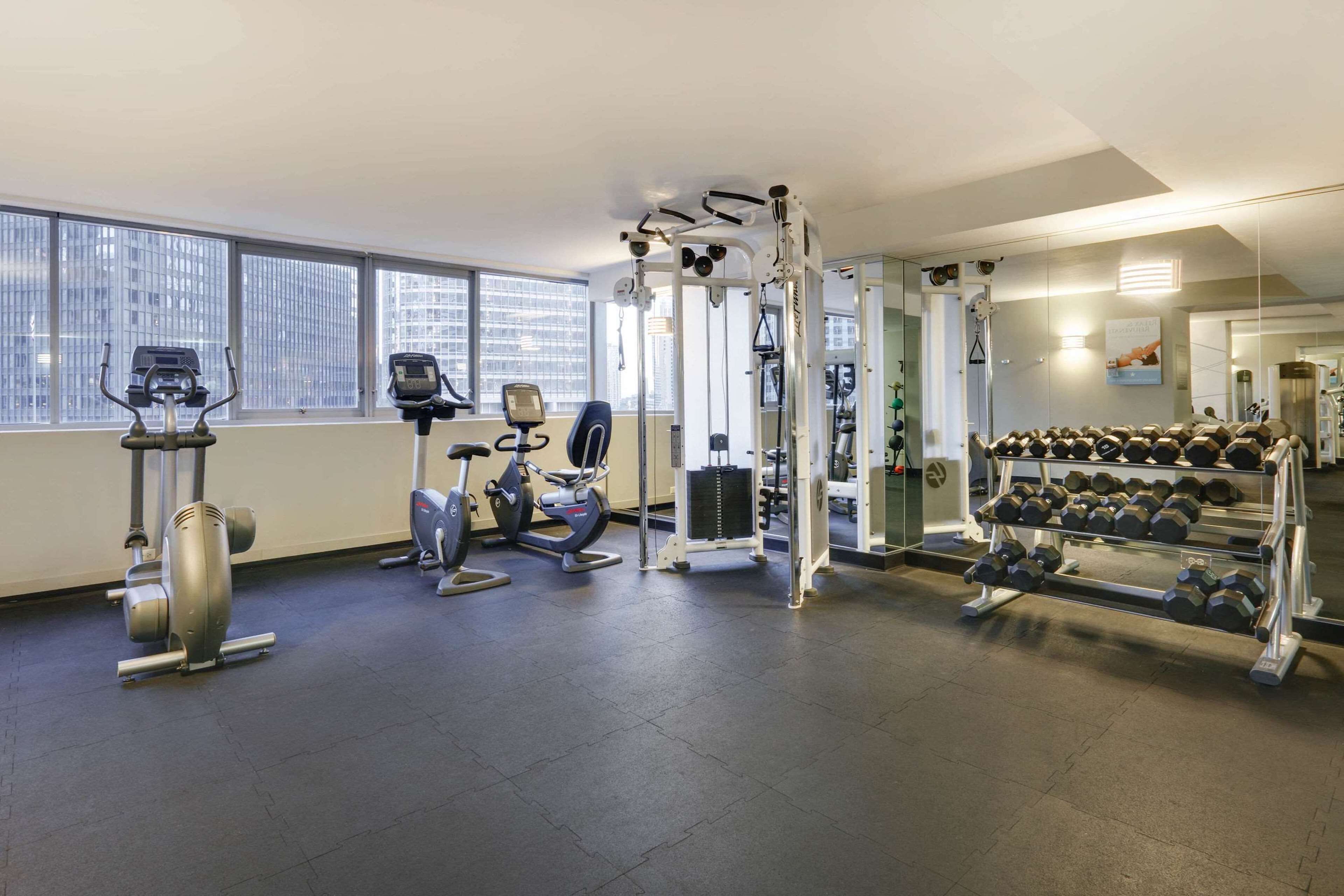 A gym with cardio machines, weightlifting equipment, and a rack of dumbbells.