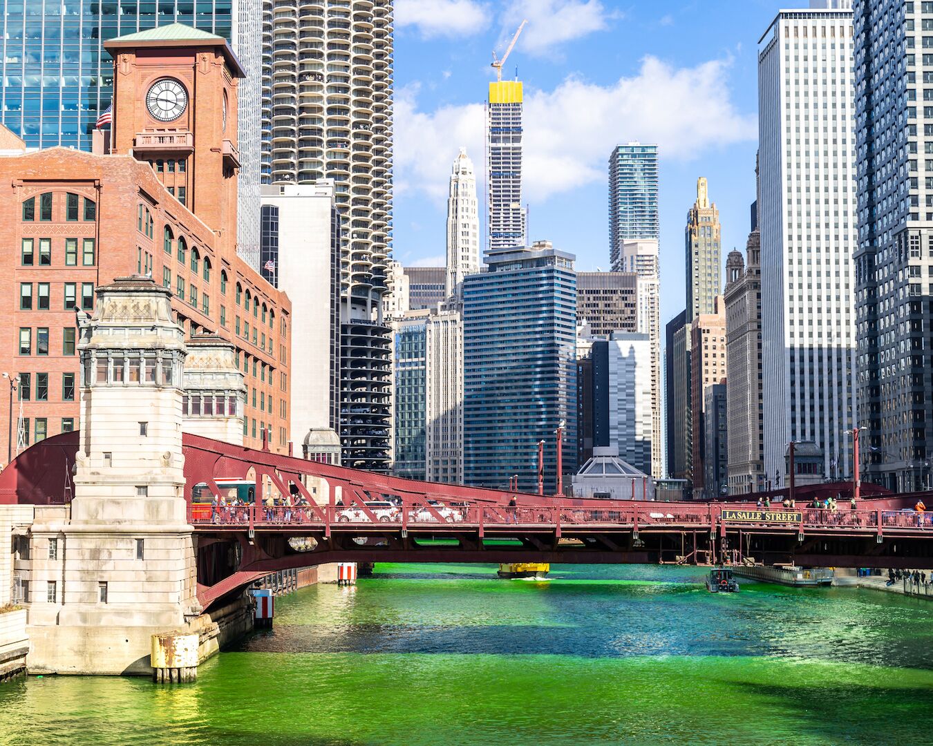A cityscape with a prominent bridge over a green river, surrounded by modern high-rise buildings.