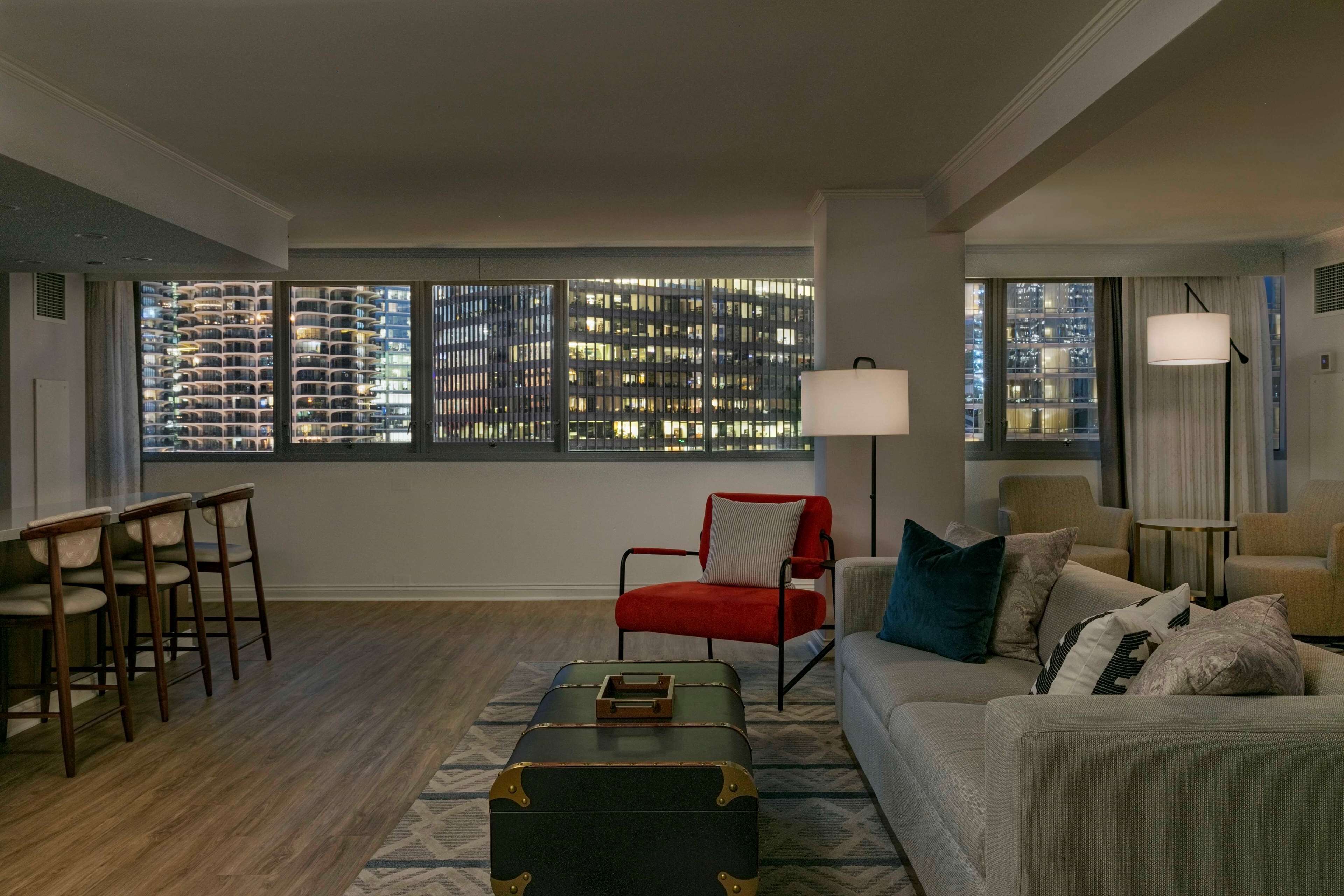 A modern living room with a city view, a red chair, a sofa, and a coffee table.