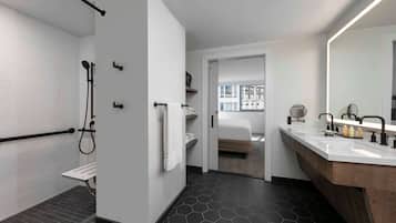 Ein modernes Badezimmer mit Dusche, Waschtisch und Spiegel, mit Blick auf ein Schlafzimmer durch eine offene Tür.