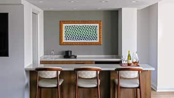 Una cocina moderna con encimera blanca, tres taburetes de madera y un marco con un motivo geométrico en la pared.