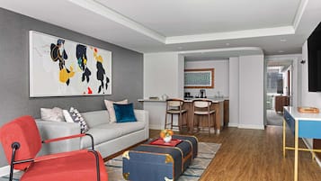 Un salon moderne avec un canapé gris, un fauteuil rouge et noir, un pouf bleu et un coin repas comprenant des chaises et une table en bois.