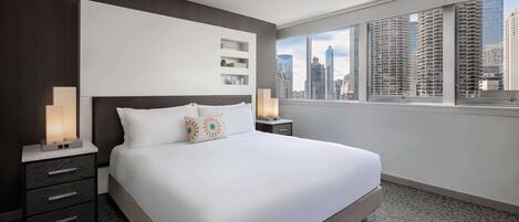 A modern hotel room with a large bed, dark wood paneling, a city view, and a nightstand with a lamp.