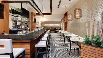 Un restaurante moderno con una barra larga, zona de bar y varias mesas para comer.
