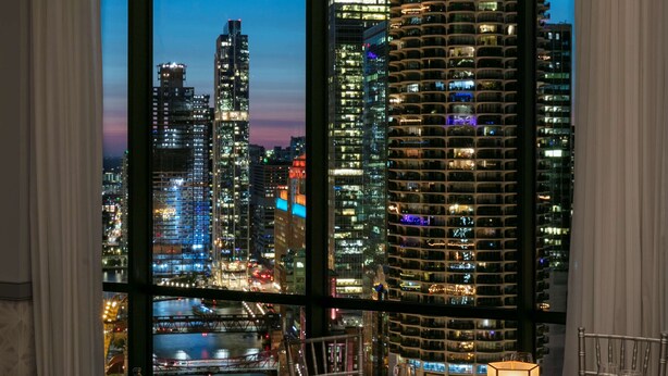 A dining area with a table set for four, large windows offering a cityscape view at dusk. - The Royal Sonesta Chicago Downtown (Chicago)