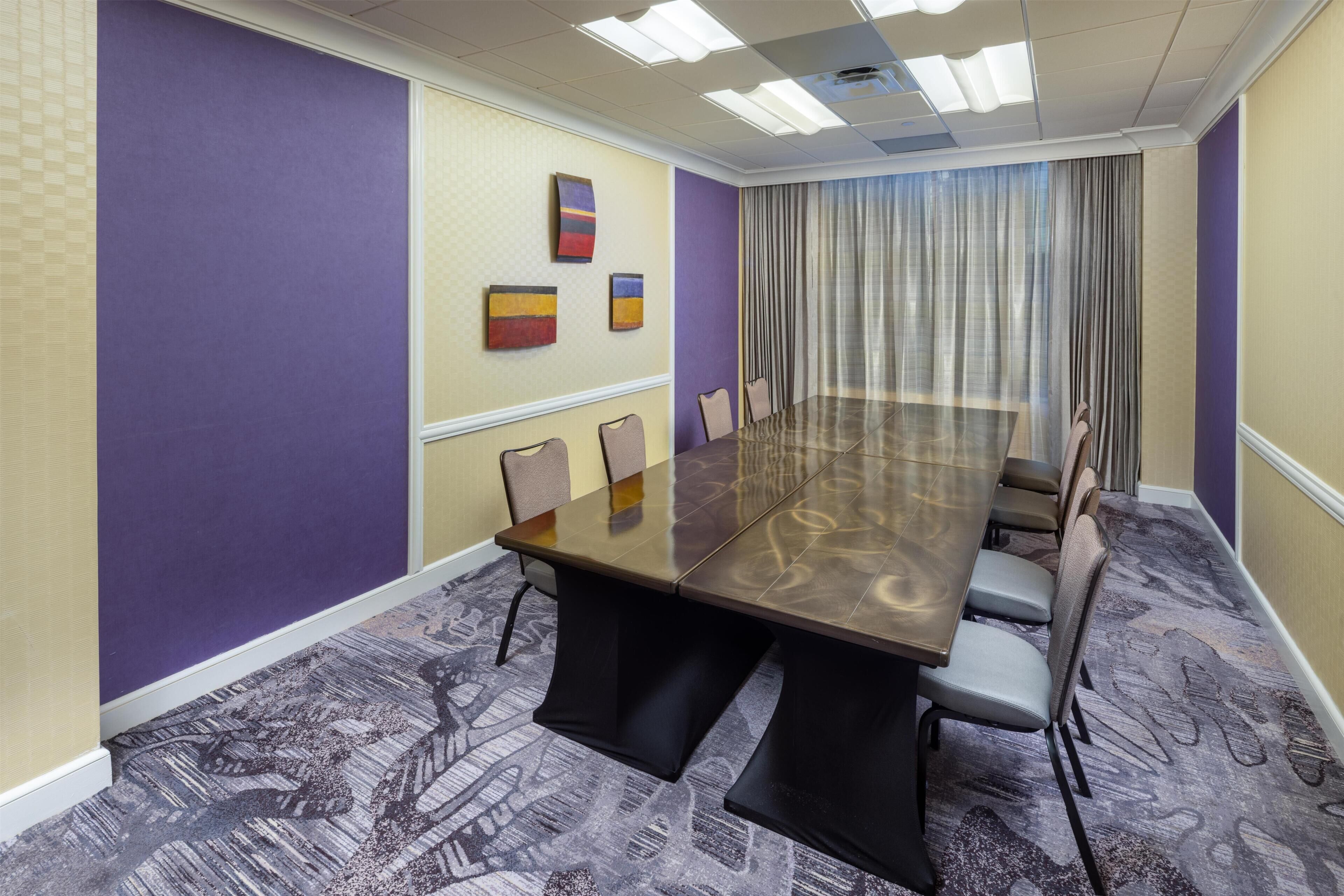 Un salón de conferencias con una mesa larga, sillas y una alfombra estampada.