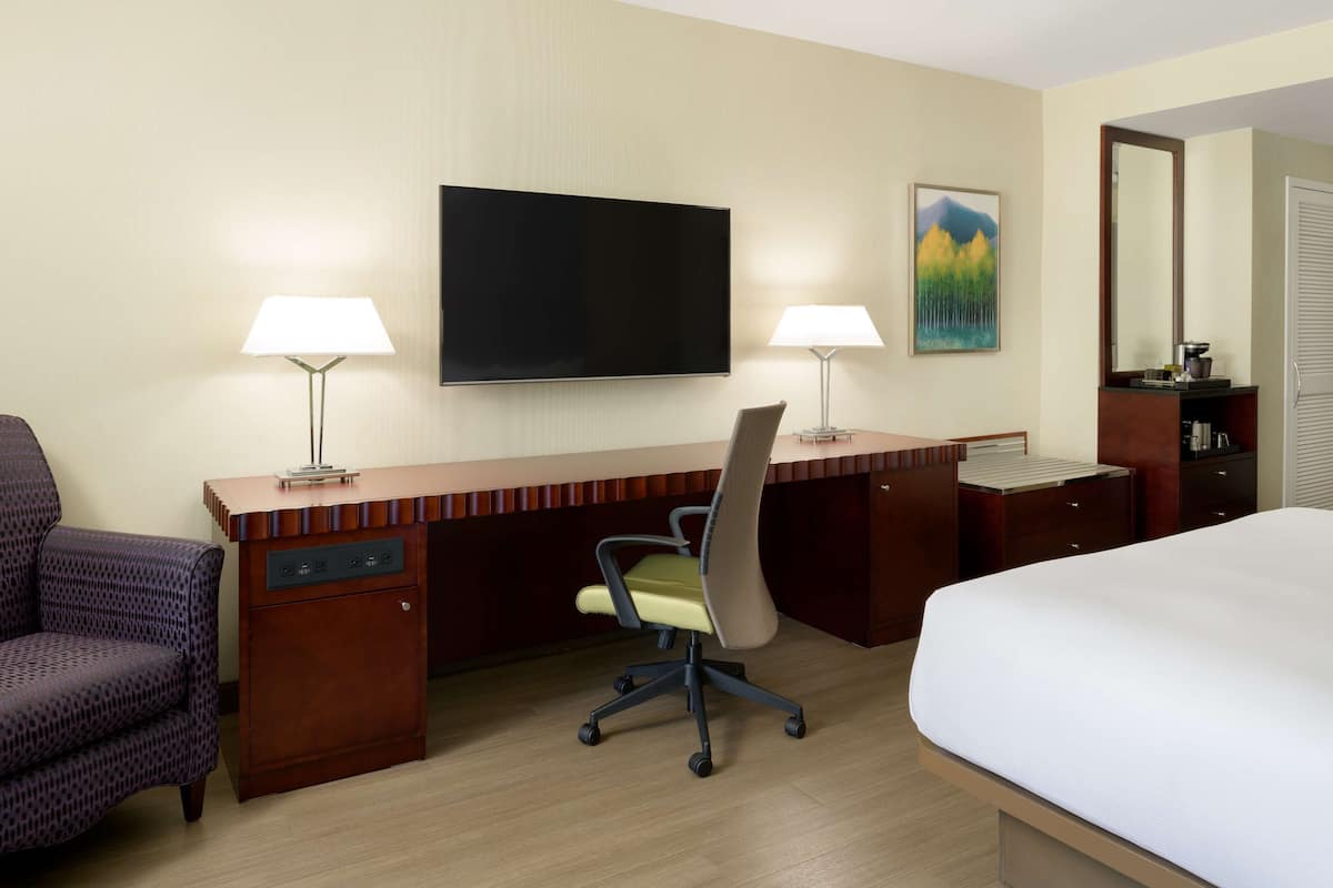 A hotel room with a large bed, a desk with two lamps, a TV, and a painting on the wall.