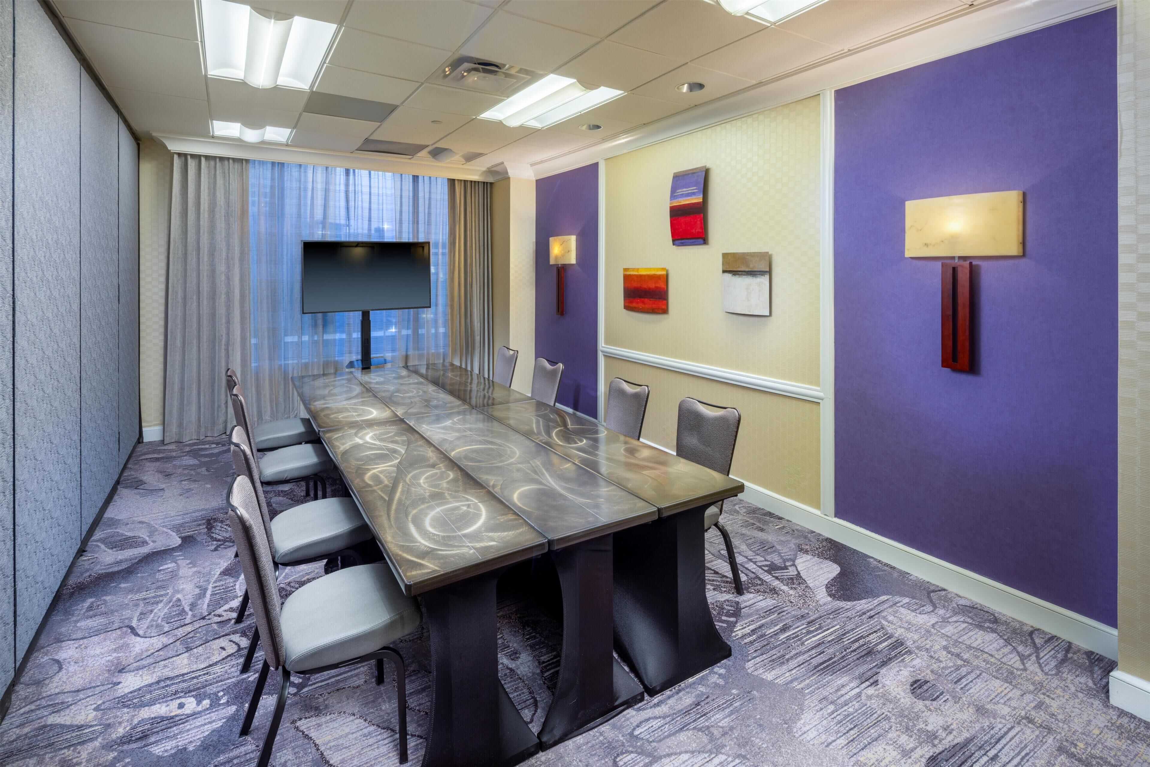 A conference room with a long table, chairs, a TV, and wall art.