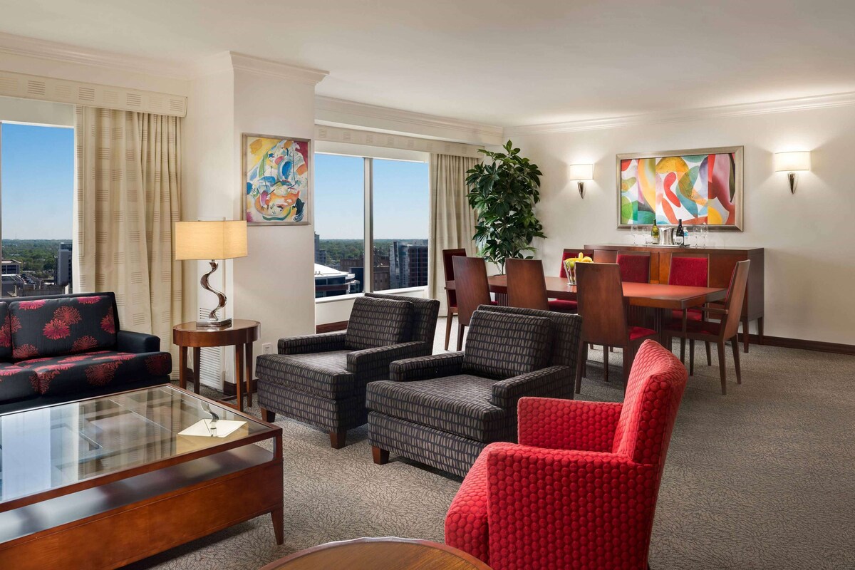 A hotel room with a seating area, a dining table, and artwork on the walls.