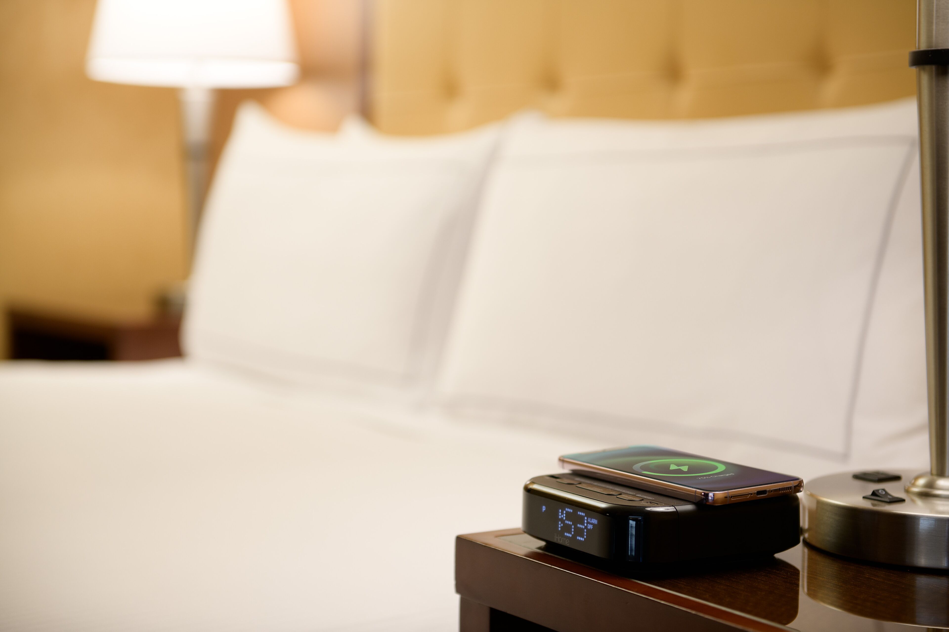 A bed with white linens and a digital clock displaying the time.
