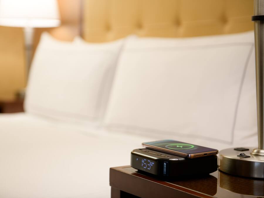 A bed with white linens and a digital clock displaying the time.