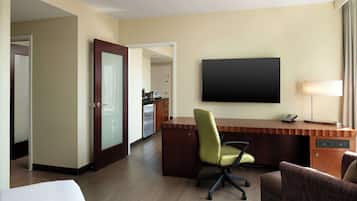 A hotel room with a wooden desk, a green office chair, a flat-screen TV, a lamp, and a bed.