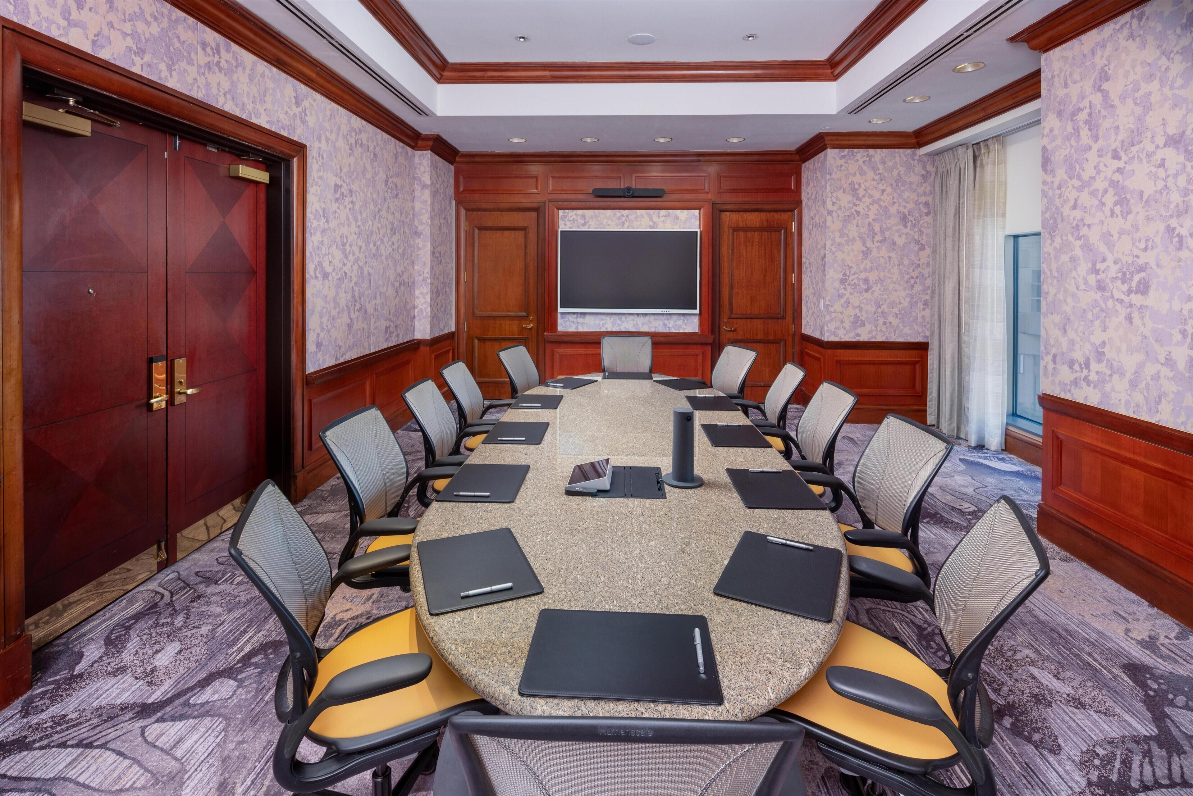 Un salón de conferencias con una mesa redonda, sillas, una pantalla de proyector y una puerta de madera grande.