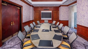 A conference room with a round table, chairs, a projector screen, and a large wooden door.