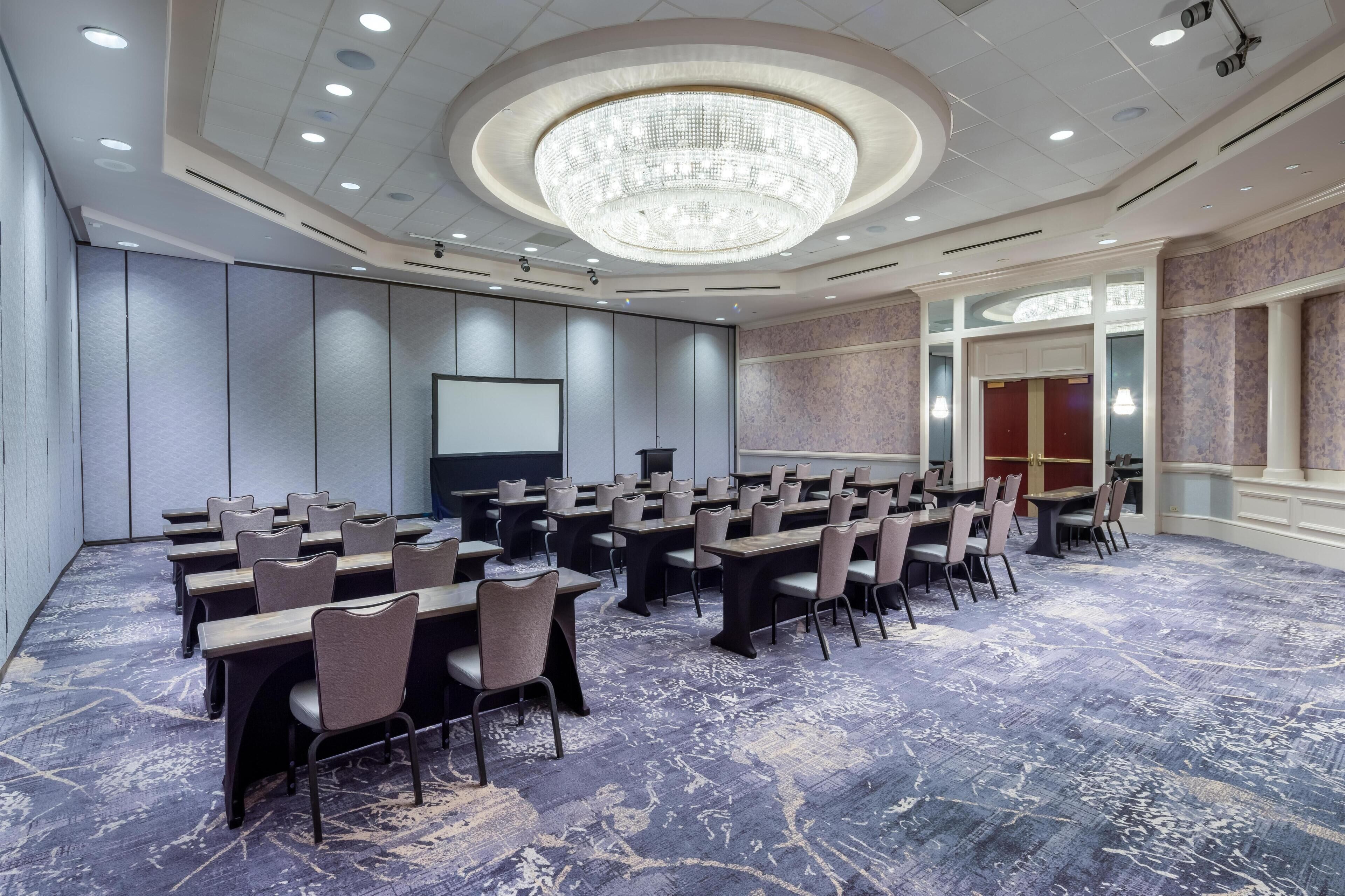 A conference room with tables and chairs, a large chandelier, and a projector screen.