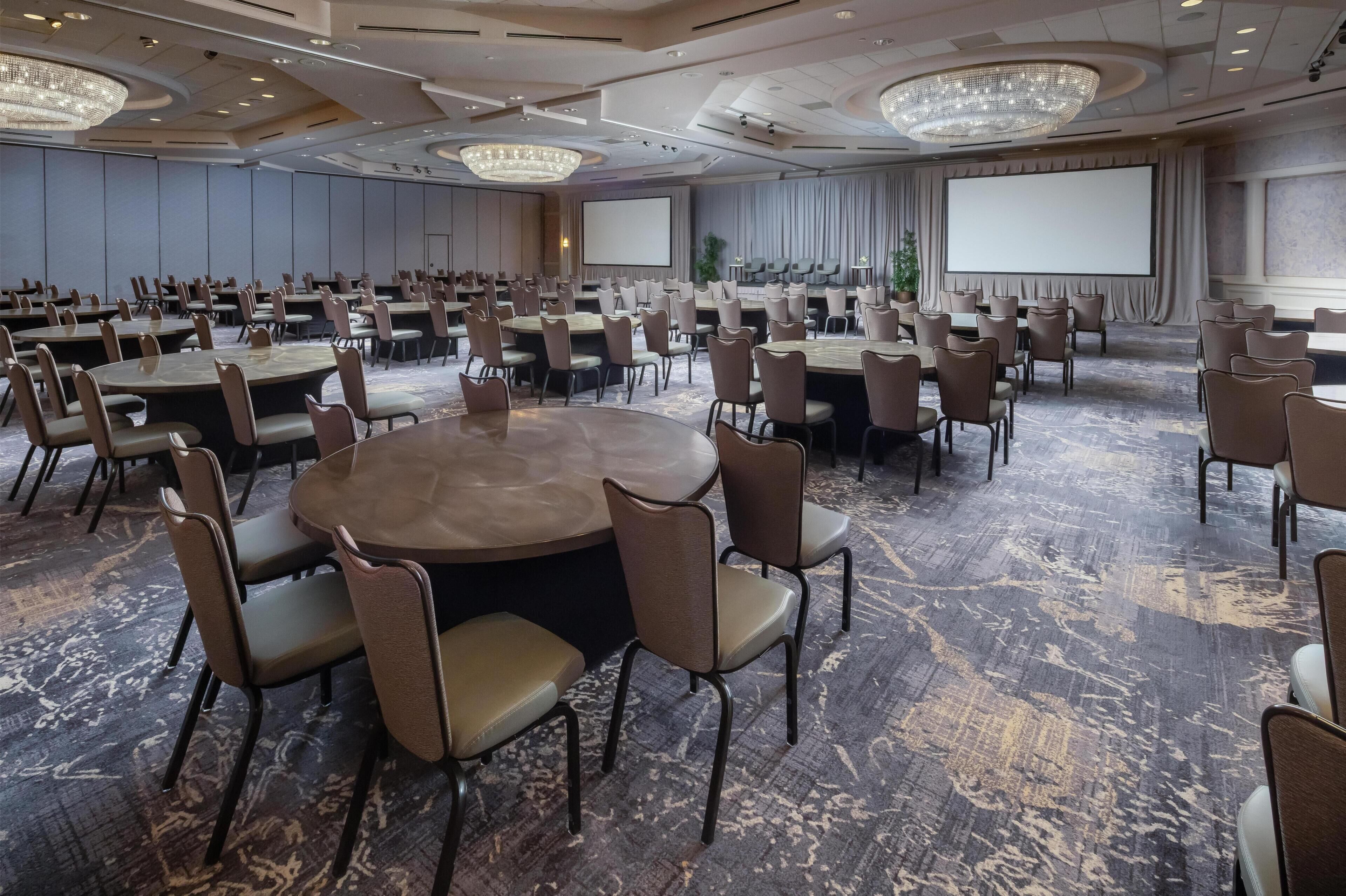 A conference room with round tables, chairs, a large screen, and a carpeted floor.