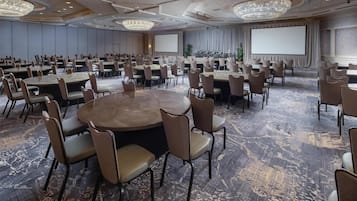 A conference room with round tables, chairs, a large screen, and a carpeted floor.