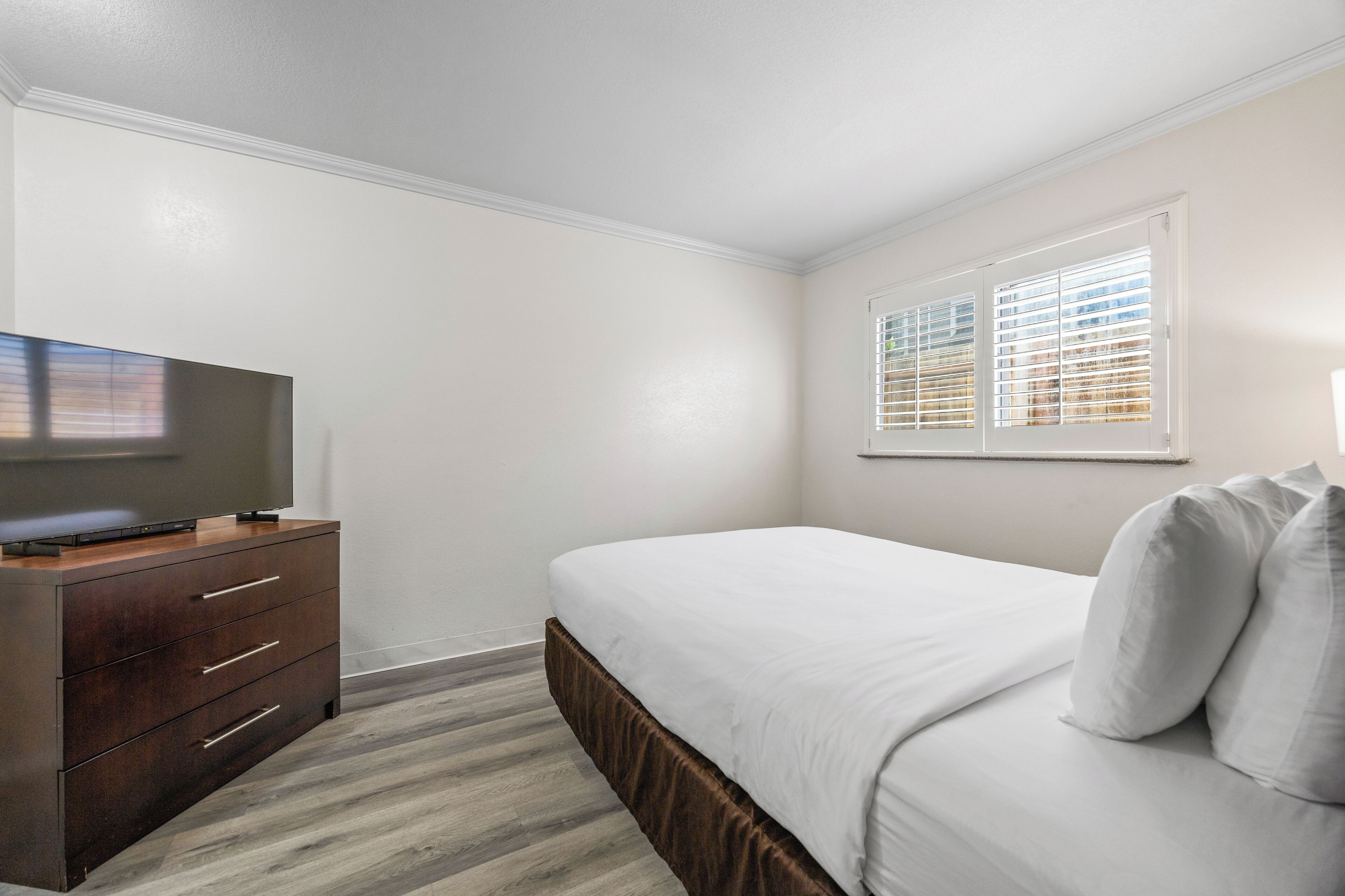 A bedroom with a bed, a dresser, a television, and a window with blinds.