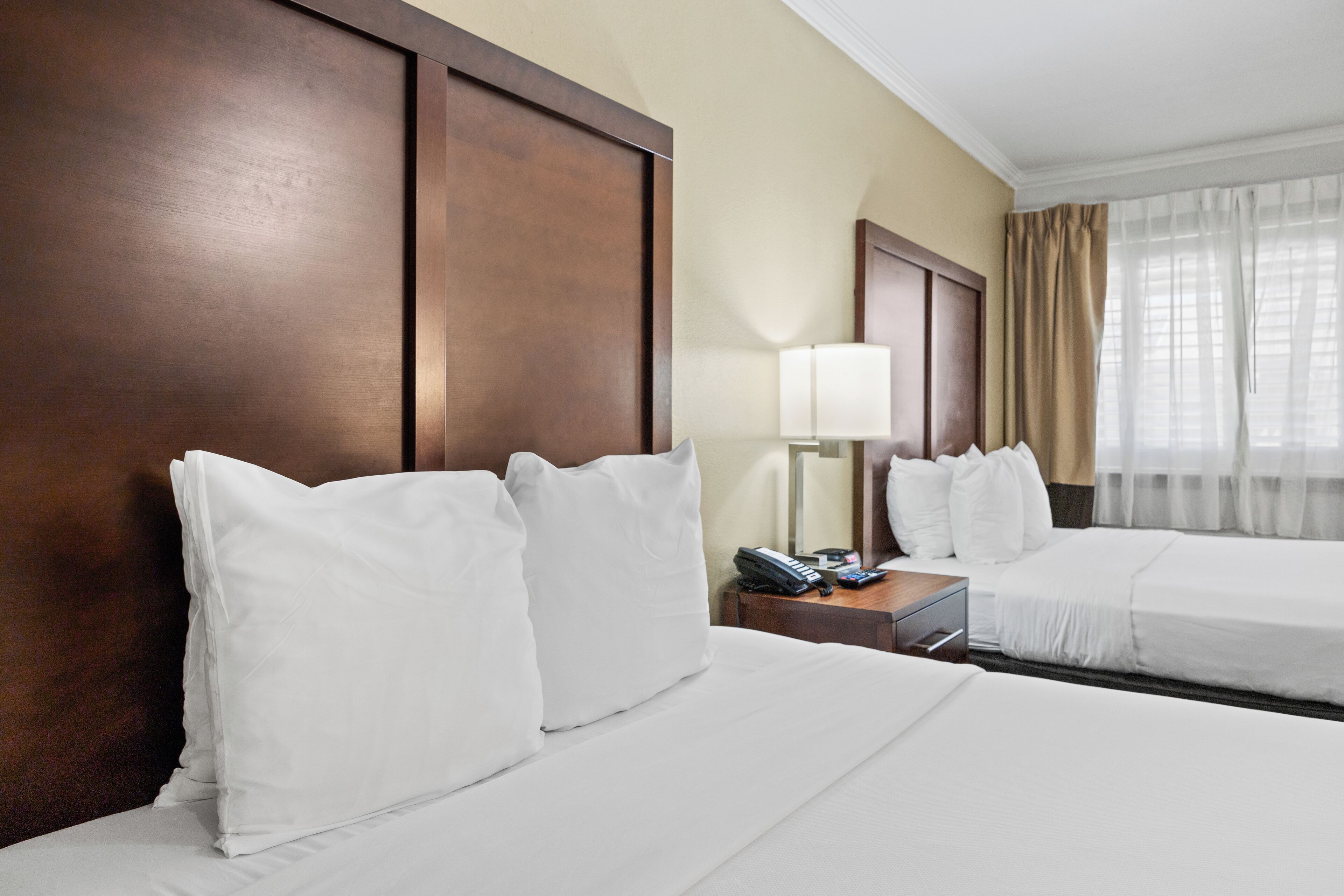 A hotel room with two beds, a nightstand with a lamp, and a window with curtains.
