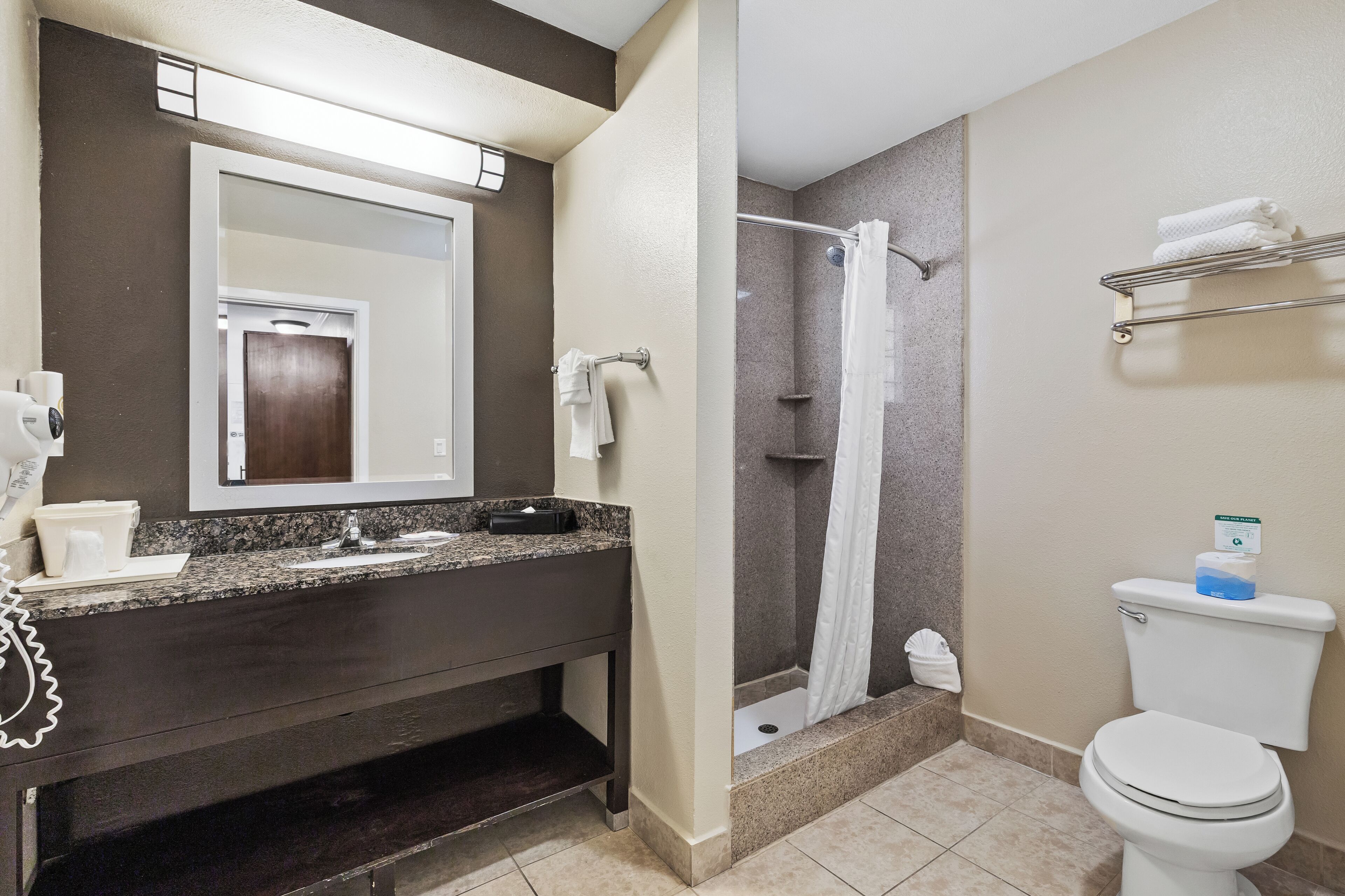 A bathroom with a dark vanity, a white toilet, a shower with a curtain, and a towel rack.