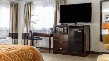 A hotel room with a bed, a desk with a television, a minibar, and a chair.