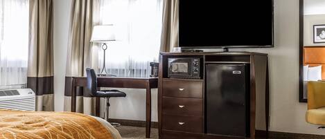 Una habitación de hotel con una cama, un escritorio con televisor, un minibar y una silla.