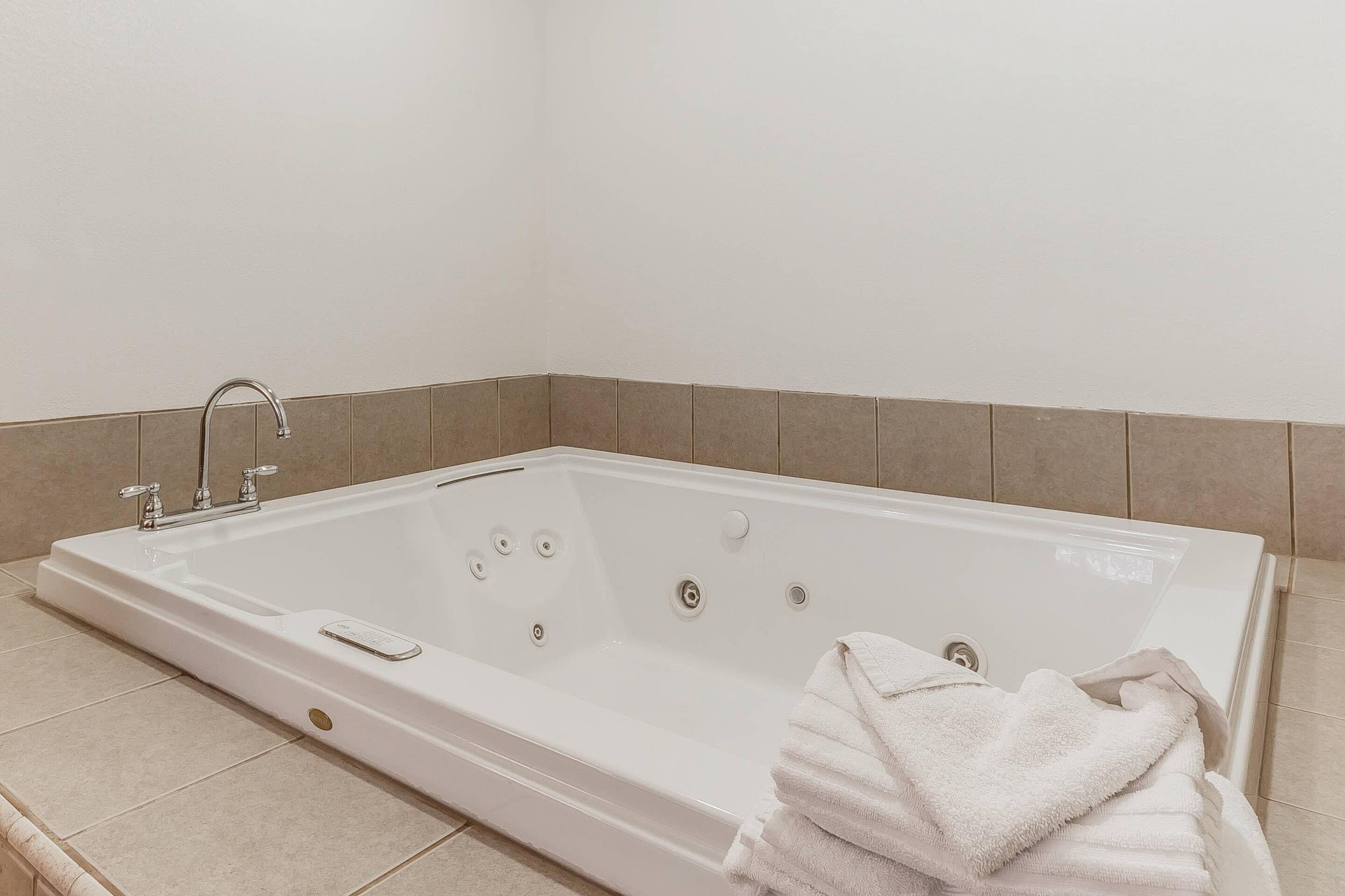 A large, rectangular bathtub with a faucet and multiple jets, a towel rack, and a tiled floor.