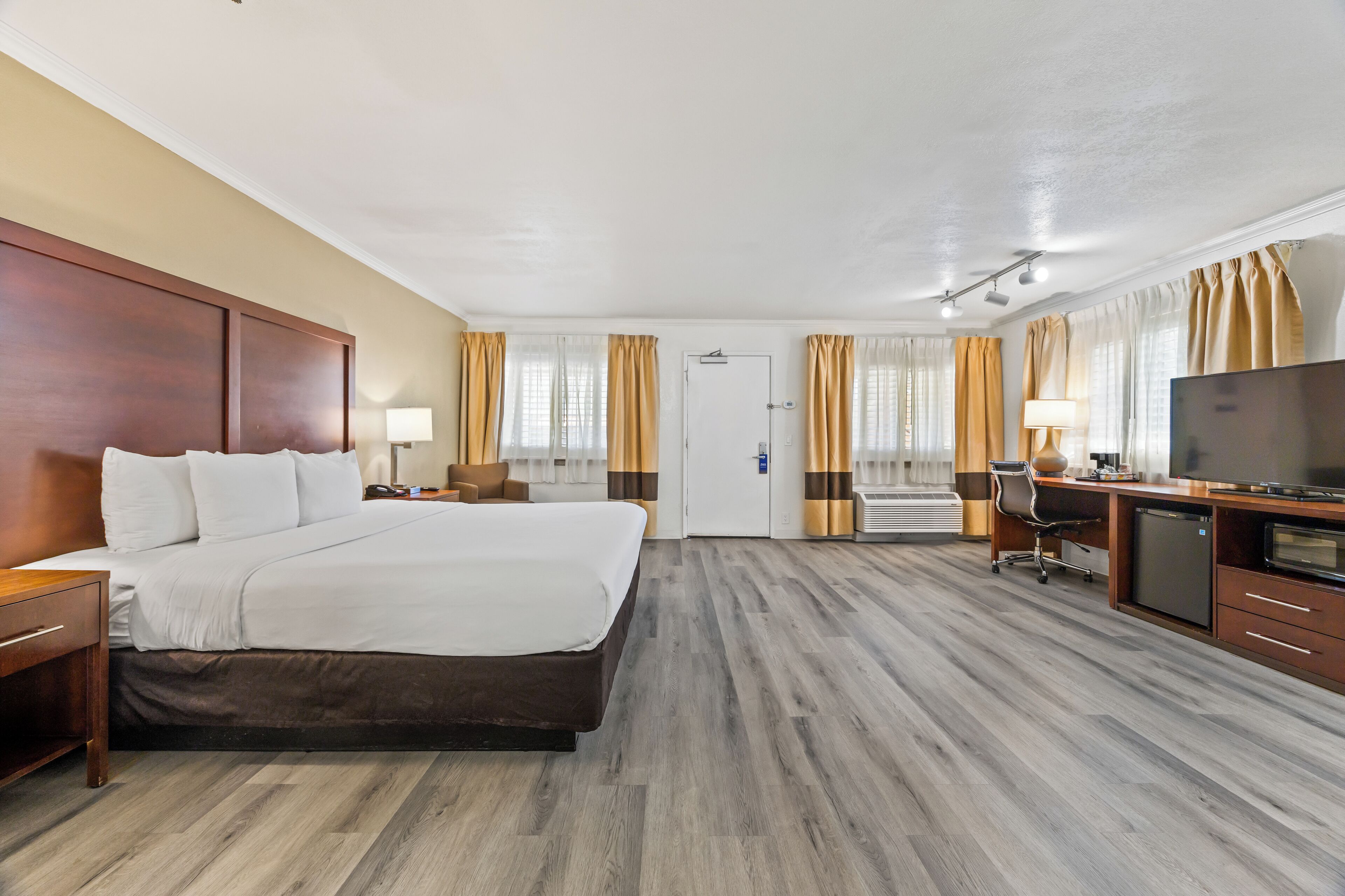A hotel room with a large bed, a desk with a television, and a chair.