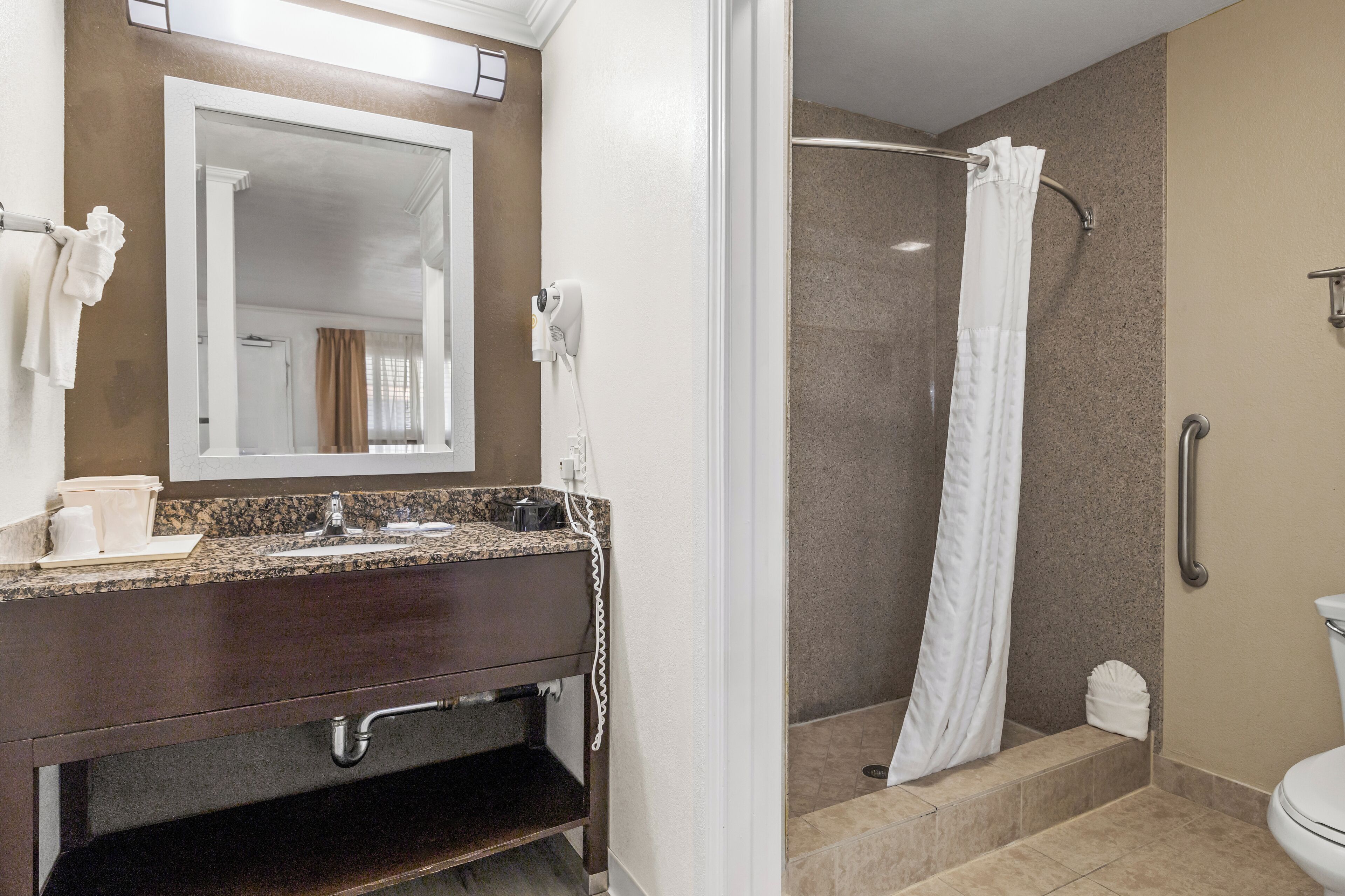 A bathroom with a granite countertop, a mirror, a towel rack, a shower with a curtain, and a toilet.