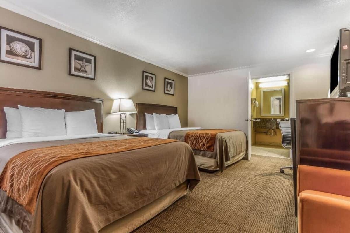 Ein Hotelzimmer mit zwei Betten, einem Schreibtisch, einem Sessel und einem Fernseher.
